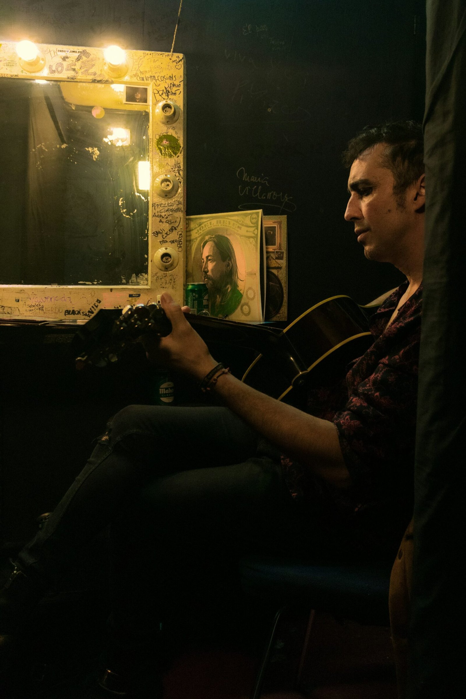 a man sitting in front of a mirror holding a guitar